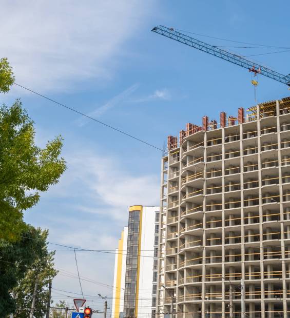 Concrete frame of tall apartment building under construction and tower crane in a city.